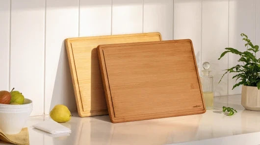 Natural and carbonized bamboo cutting board sets compared side by side in a bright kitchen