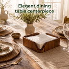 Wooden napkin holder with white paper napkins on a dining table set with plates and glassware